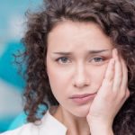 young woman holds her jaw with pain