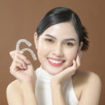 girl with black hair and a beautiful smile holds in hand invisalign