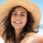 cheerful girl on the beach holds a hat on head