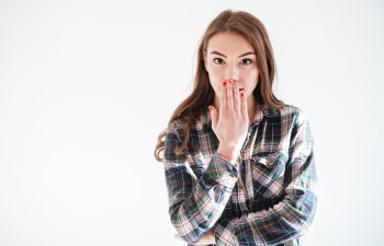 Happy amazed young woman covered her mouth by hand over white background